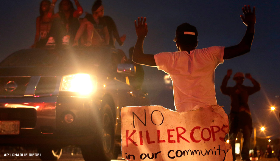 People protest Sunday, Aug. 17, 2014, for Michael Brown, who was killed by a police officer last Saturday in Ferguson, Mo. As night fell Sunday in Ferguson, another peaceful protest quickly deteriorated after marchers pushed toward one end of a street. Police attempted to push them back by firing tear gas and shouting over a bullhorn that the protest was no longer peaceful.