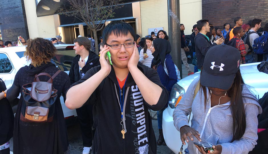 Community College of Philadelphia freshman Matthew Liu makes a phone call as students and staff gather on Spring Garden Street. Photo | Jared Shelly