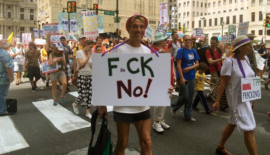 A man holds a FraCK NO! sign while walking on Market Street during an environmental protest