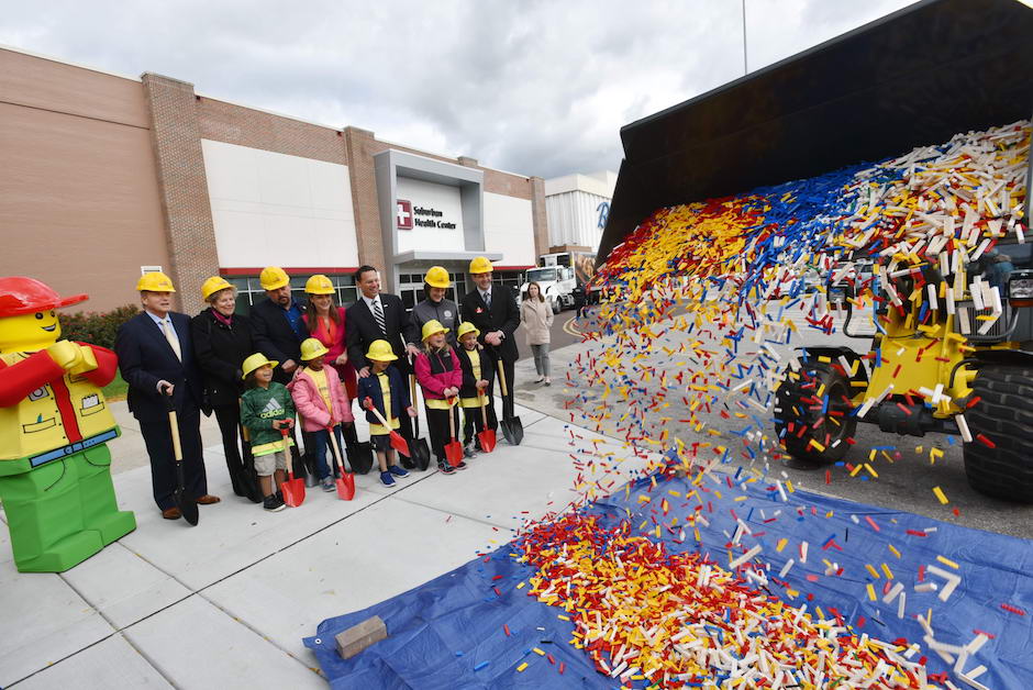 Legoland, PREIT and local elected officials and first graders look on as the bricks are dumped onto the groundbreaking site. Back row, left to right: Bertie, the Legoland Discovery Center mascot; Joe Coradino, CEO, PREIT; Wendy Klinghoffer, executive director, Eastern Montgomery County Chamber of Commerce; Dean Eisenberger, chairman, Plymouth Township Council; Rachel Schwartz, special projects manager, Visit Philadelphia; Josh Shapiro, chair, Montgomery County Board of Commissioners; Dr. Valerie Arkoosh, vice chair, Montgomery County Board of Commissioners; Michael Taylor, general manager, Legoland Discovery Center Philadelphia. First grade students from Plymouth Elementary School make up the front row. | Photo: Courtesy Legoland Discovery Center