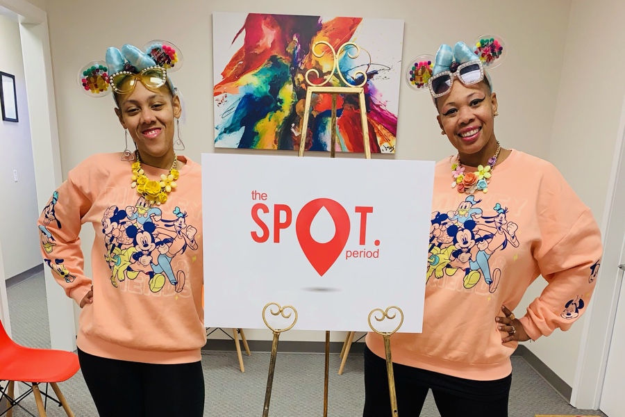 Lynette and Nya in front of a sign that says The SPOT Period